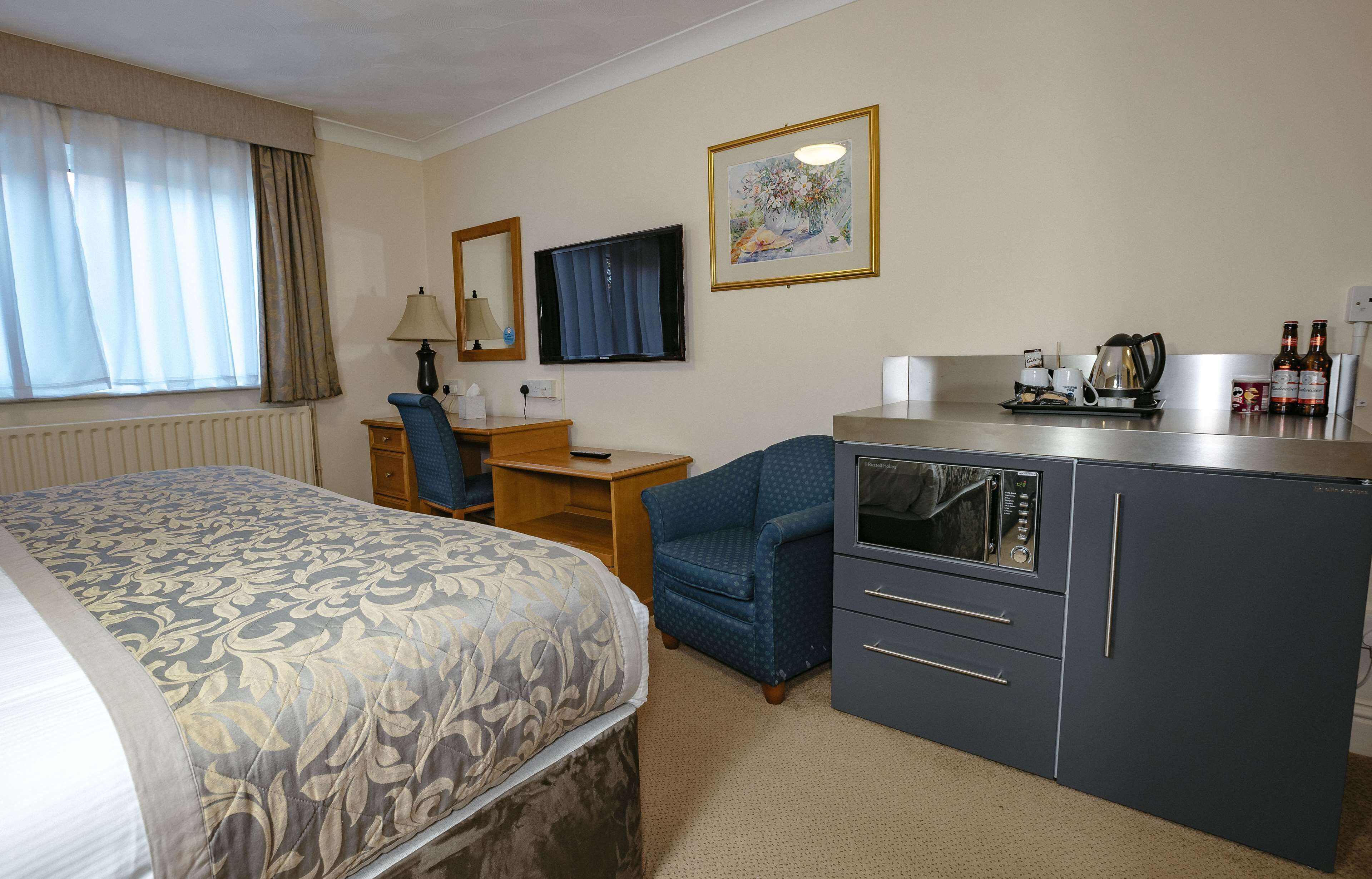 Habitación de hotel con cama, escritorio con computadora, silla, microondas y una pequeña kitchenette.
