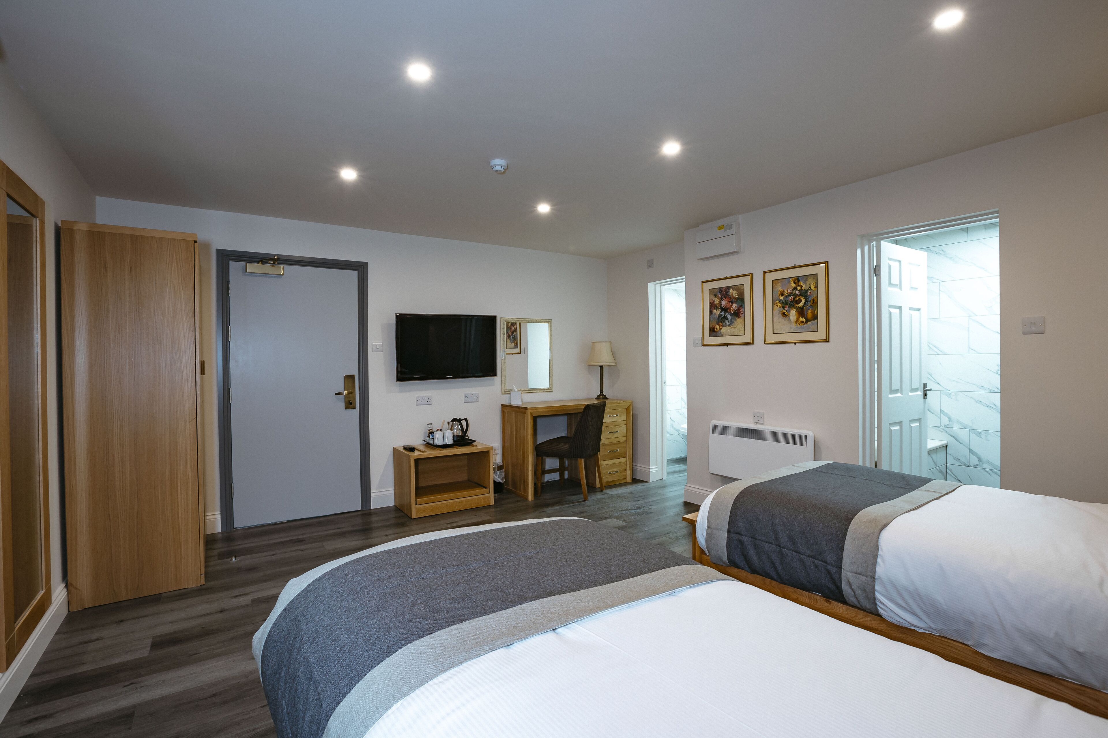 A hotel room with two beds, a desk with a chair, a TV, and artwork on the wall.