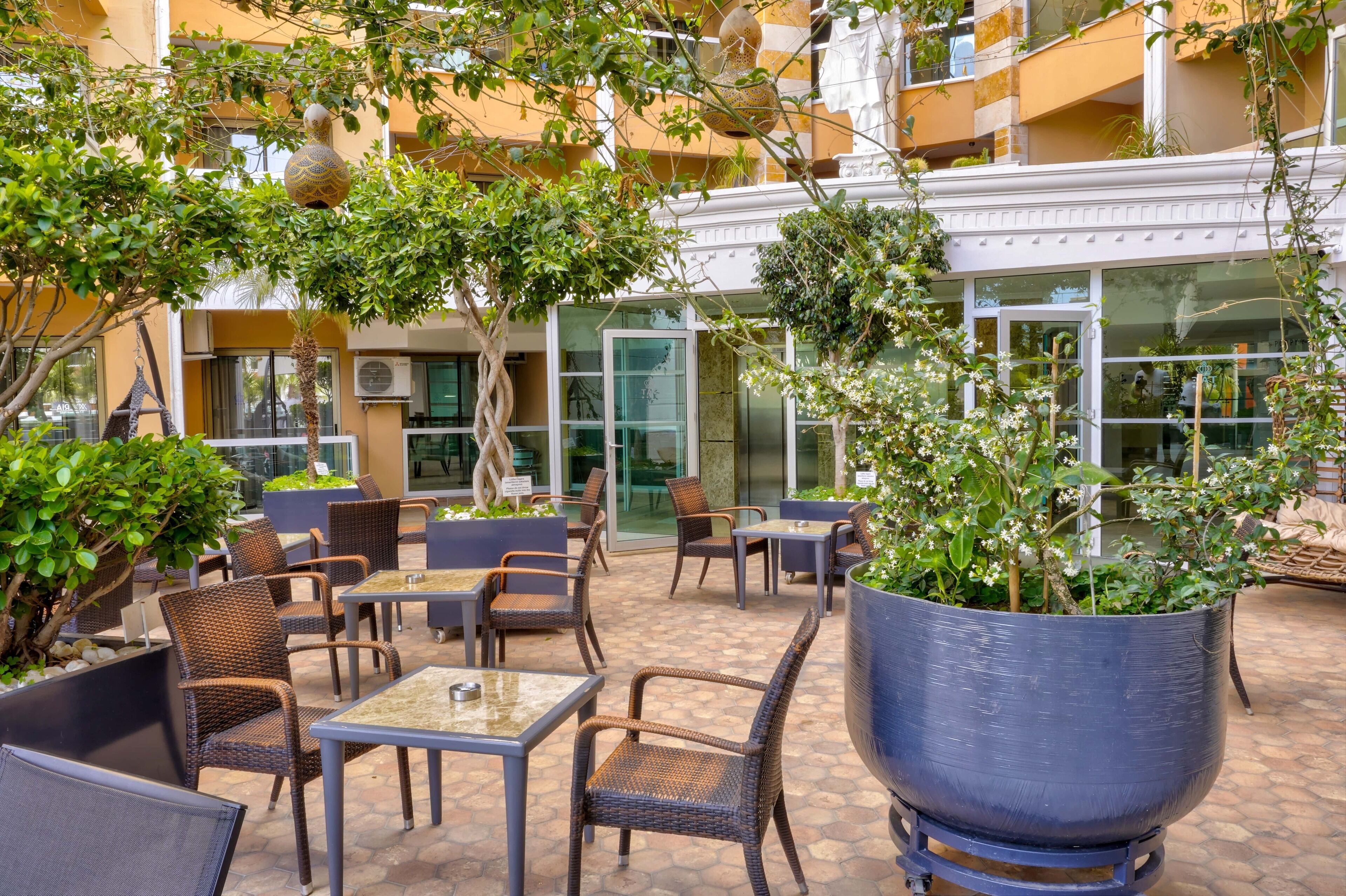 Un patio al aire libre con mobiliario de mimbre, plantas en macetas y una jardinera grande.