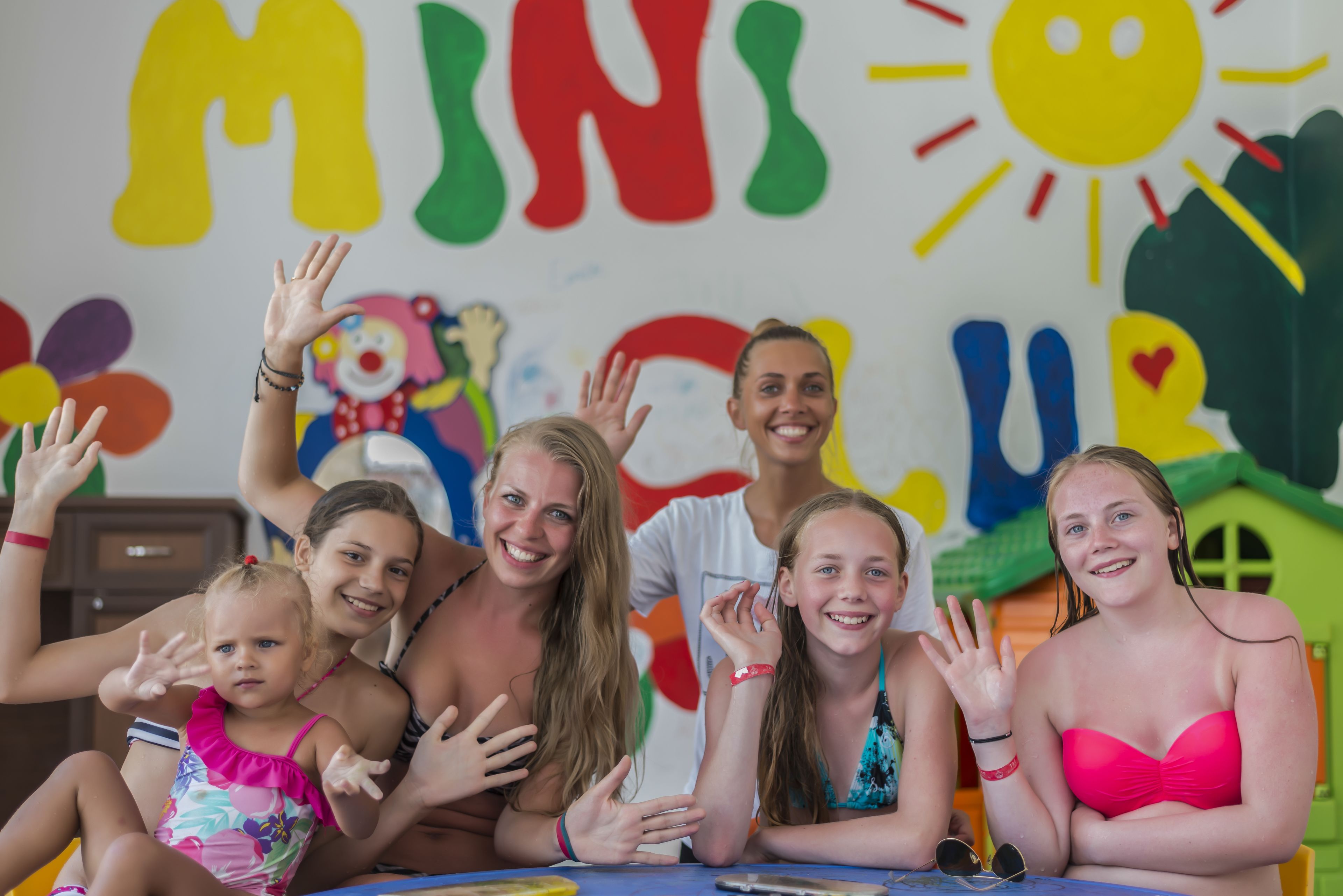 A group of people sitting at a table with a colorful wall in the background.