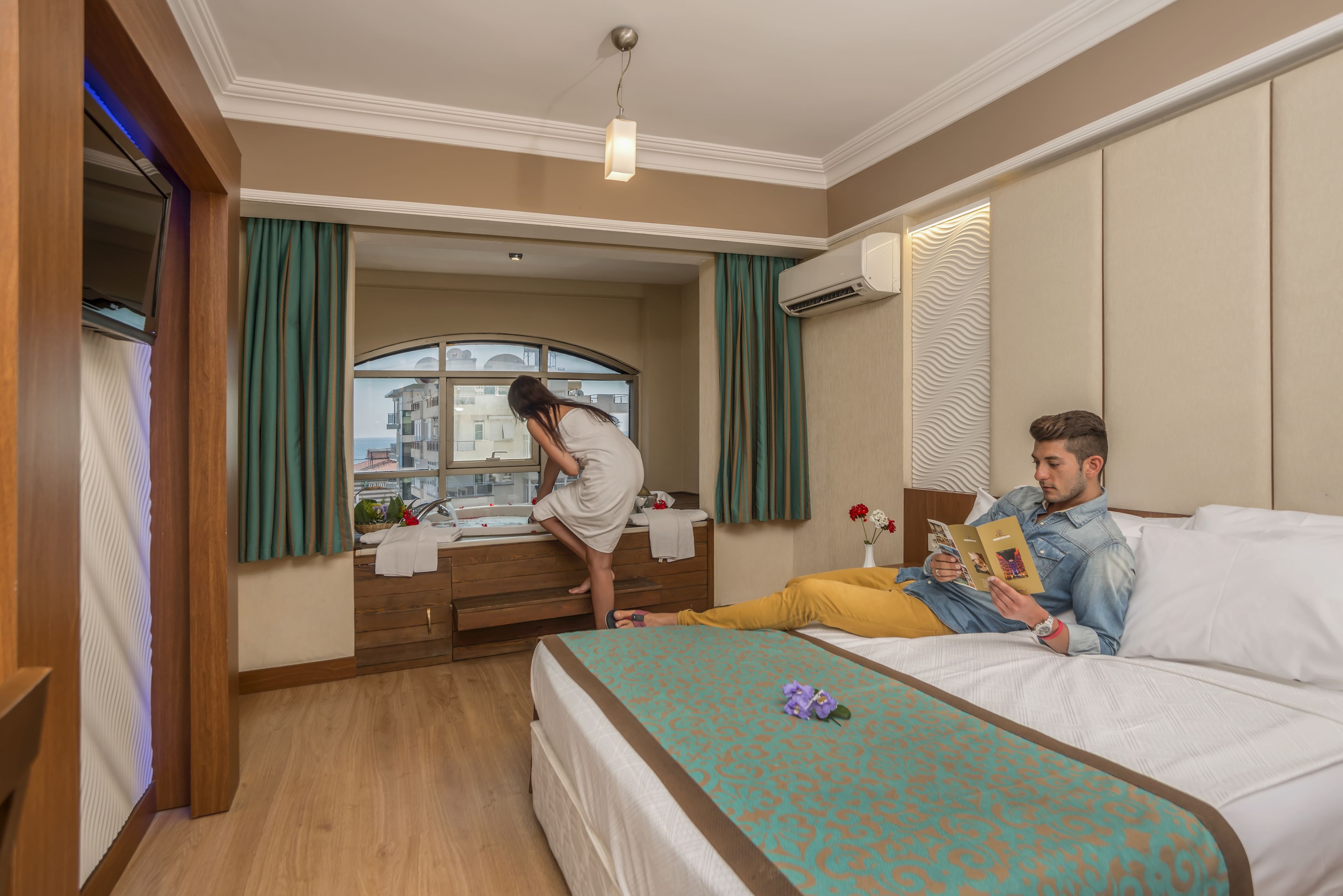 Quarto de hotel com cama, banheiro com toucador e janela com cortinas.