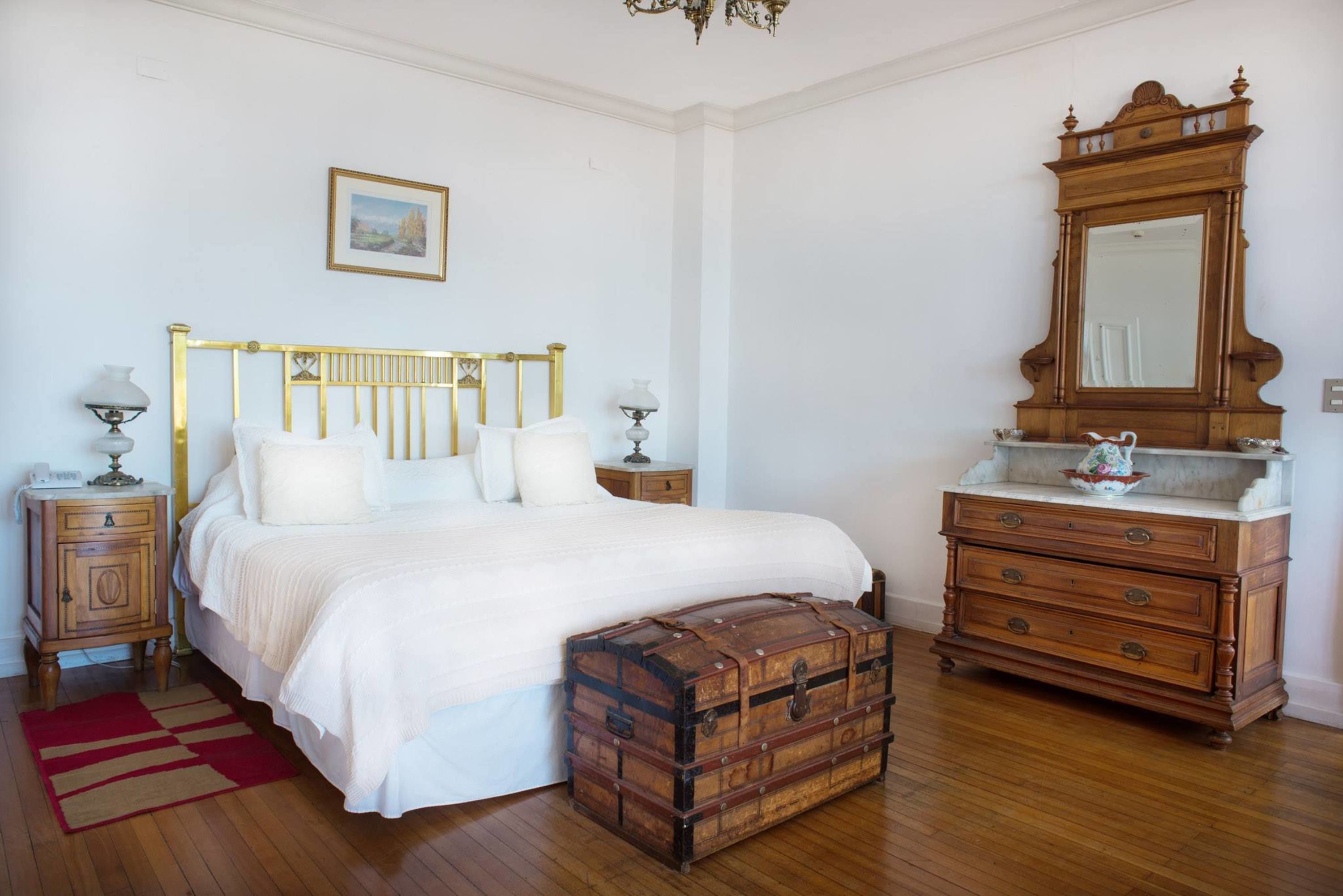 Un dormitorio con cama, cómoda de madera y un baúl antiguo.