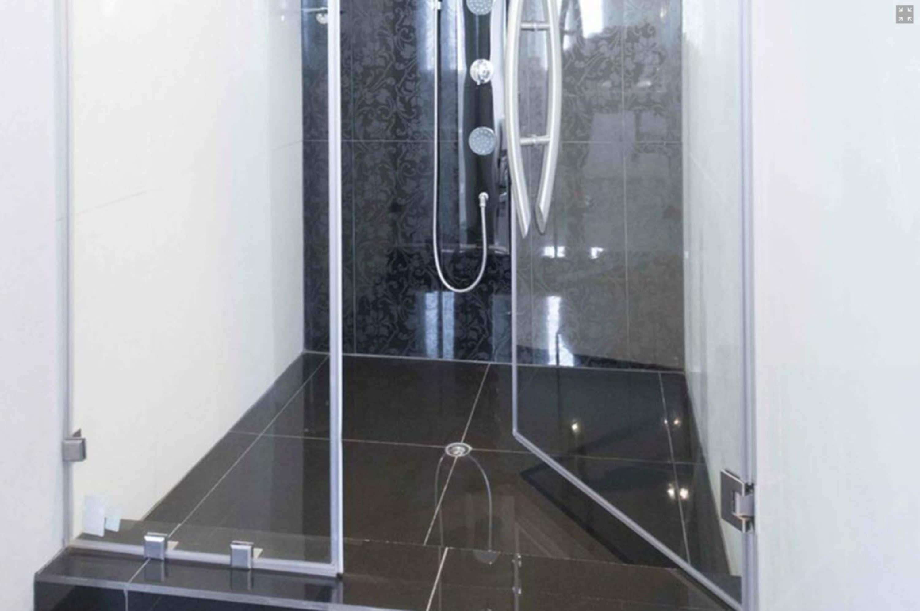 Box de chuveiro moderno com porta de vidro, piso em azulejos pretos e chuveiro aparente.