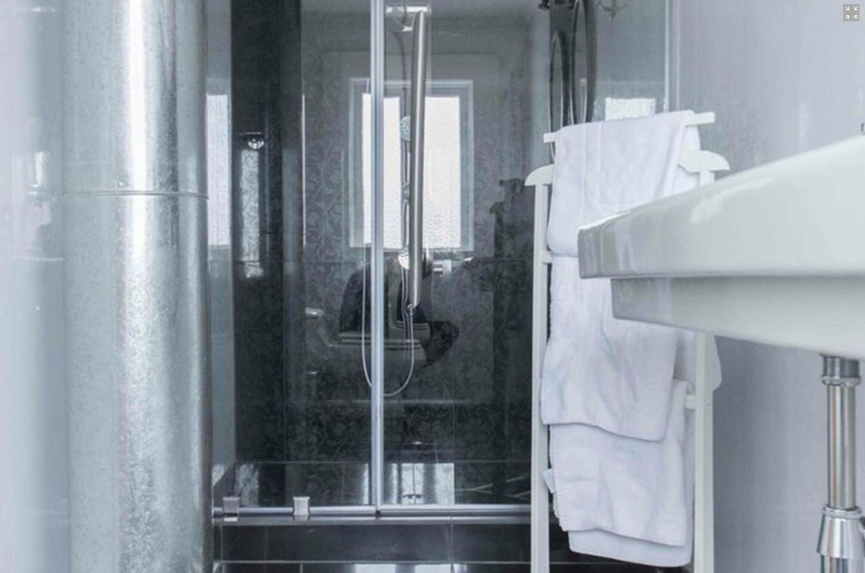 A modern bathroom with a glass-enclosed shower, a white sink, and a towel rack.