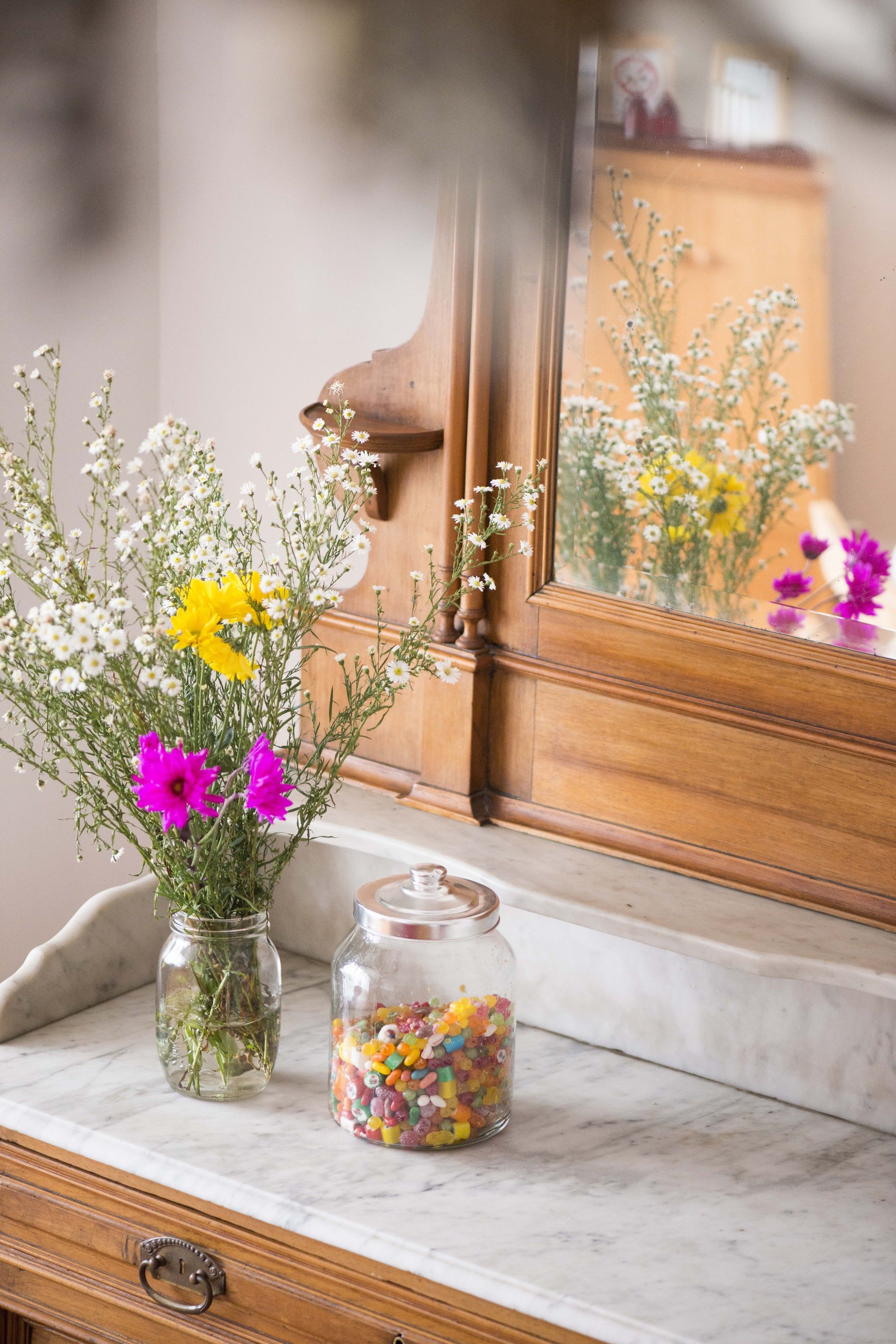 Encimera de mármol con un mueble de madera y un espejo que refleja flores.
