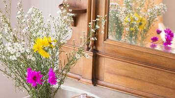 Encimera de mármol con un mueble de madera y un espejo que refleja flores.