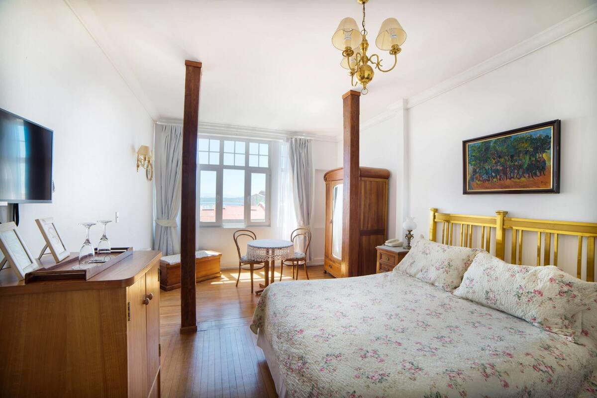 A bedroom with a bed, a wooden dresser, a TV, and a painting on the wall.