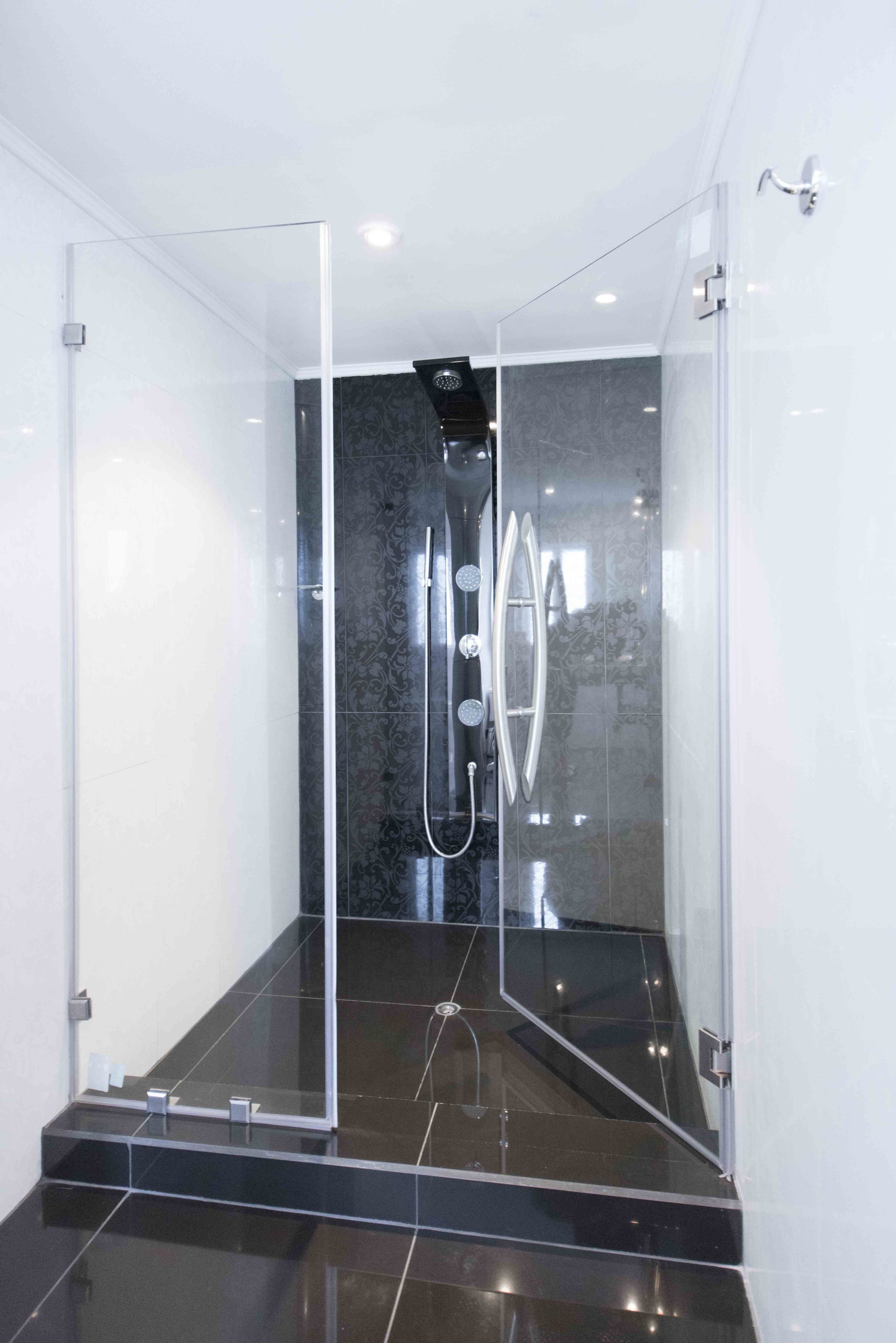 Een moderne douche met een glazen cabine, een marmeren wand en een vloer van zwarte tegels.