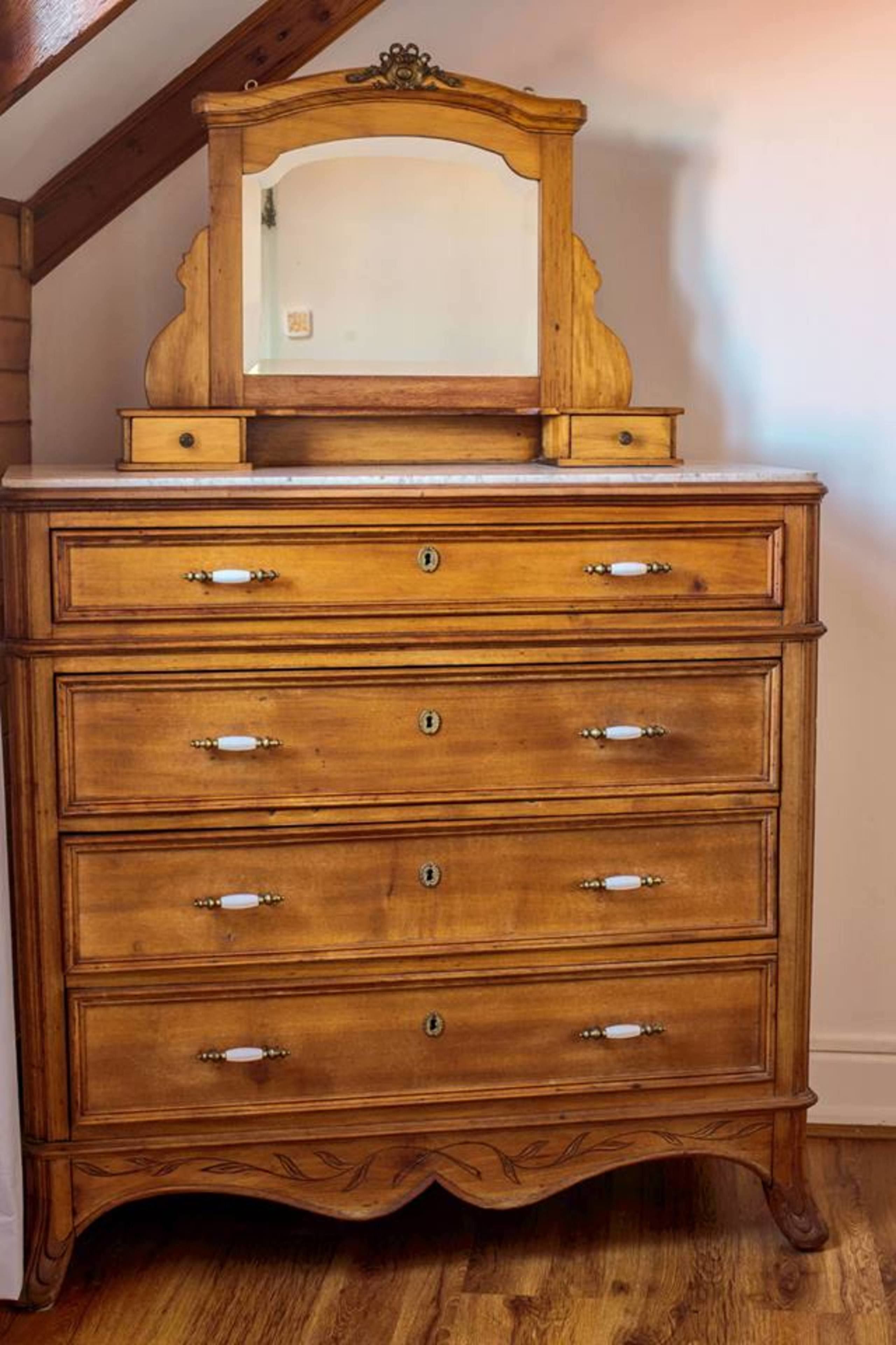 Un aparador de madera con espejo y cuatro cajones, con detalles de tallado ornamental y tiradores de latón.