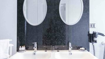 Une salle de bain avec deux lavabos, un miroir et un sèche-cheveux fixé au mur.