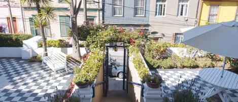 A staircase leading to a courtyard with a checkered floor, surrounded by potted plants and a bench.