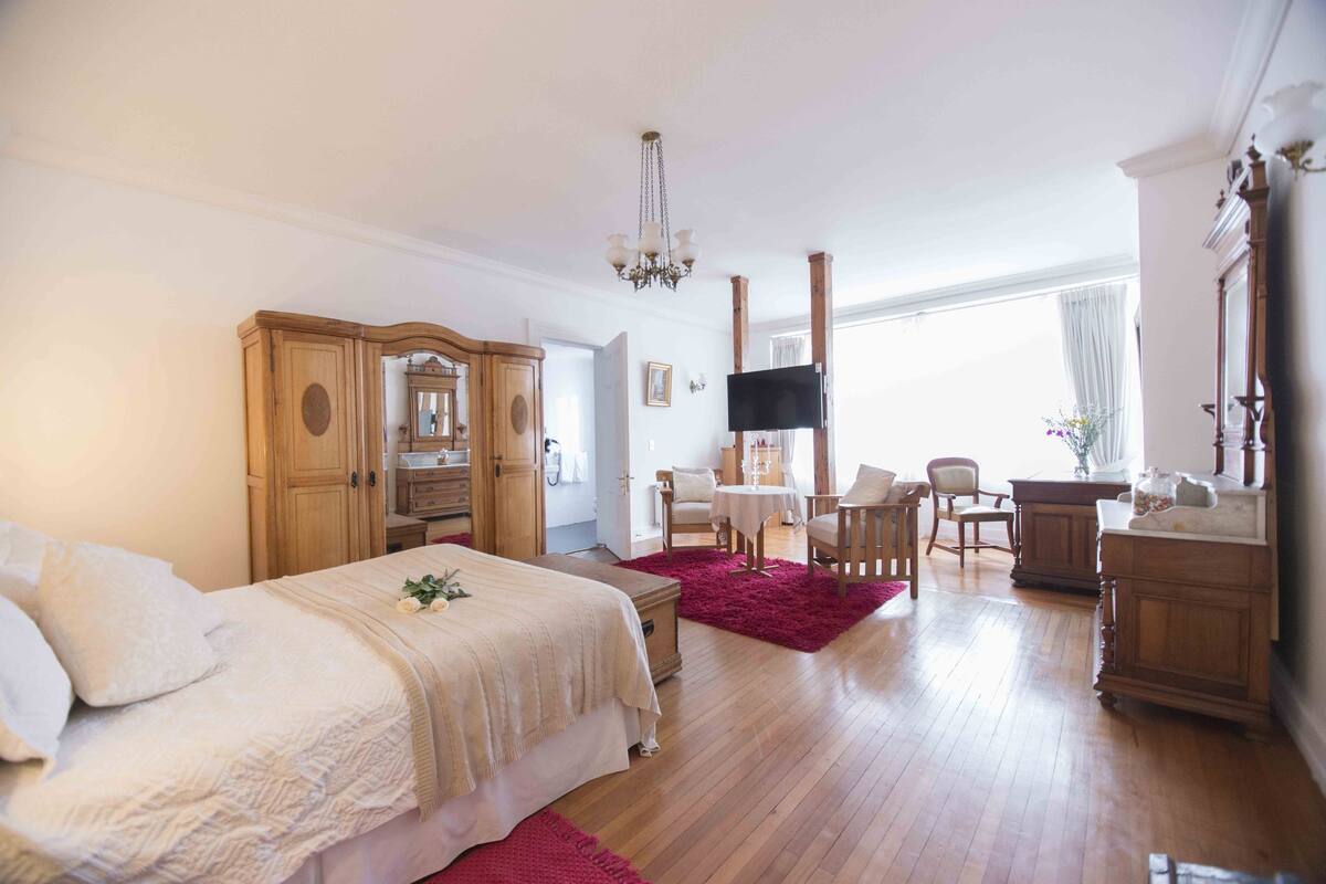 A bedroom with a bed, wooden wardrobe, TV, and a desk with chairs.