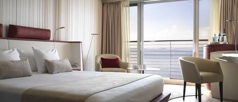 A hotel room with a large bed, a desk, a chair, and a view of the sea.