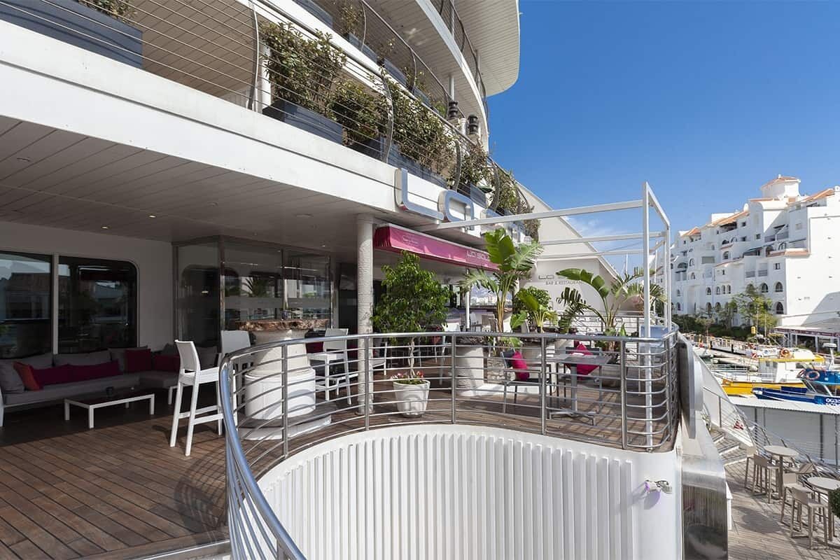 A deck with outdoor seating and a pool area, surrounded by balconies with plants.