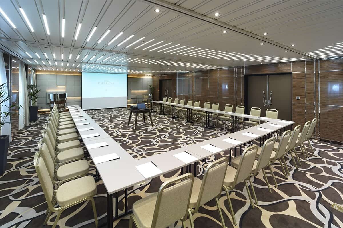 Una sala de conferencias con una mesa larga, sillas y una pantalla para proyector.