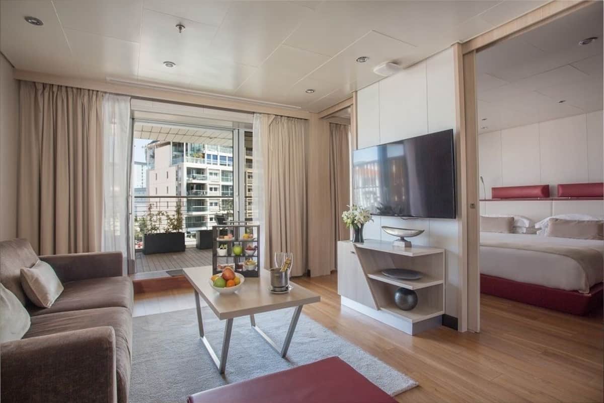 Ein modernes Hotelzimmer mit einer Couch, einem Esstisch mit Obst, einem Fernseher und einem Bett.