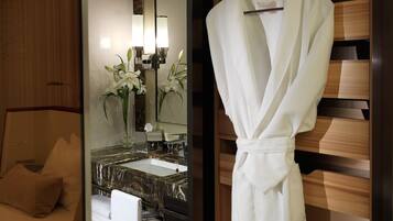 Un baño de hotel con un lavamanos de mármol, una bata blanca colgada en un perchero y un espejo con una lámpara empotrada en la pared.