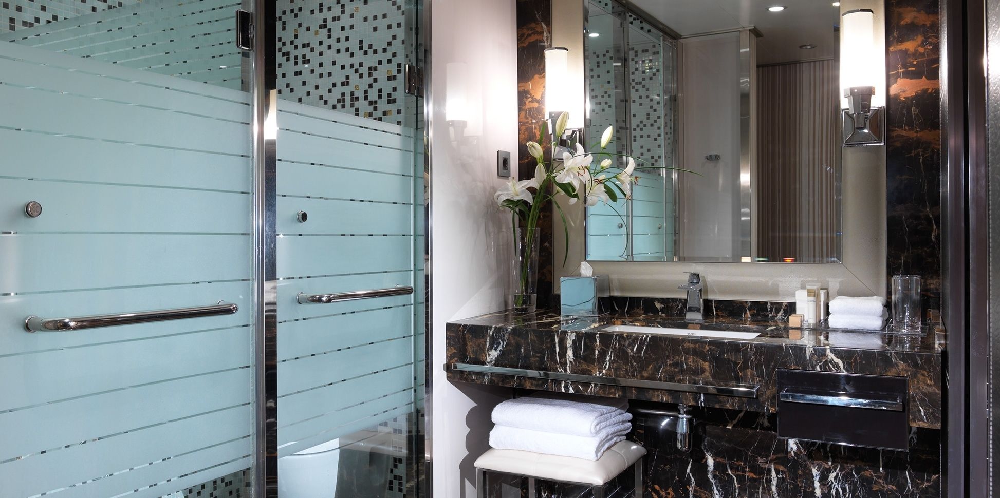 Une salle de bain moderne avec une douche à l’italienne en verre, un lavabo en marbre et un grand miroir.