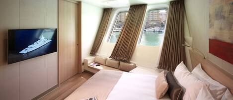 A modern hotel room with a large bed, a TV, a sofa, and a view of the water through windows.