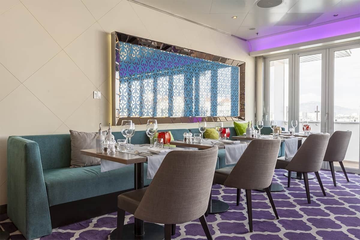 A dining area with a teal sofa, grey chairs, and a table set for four.