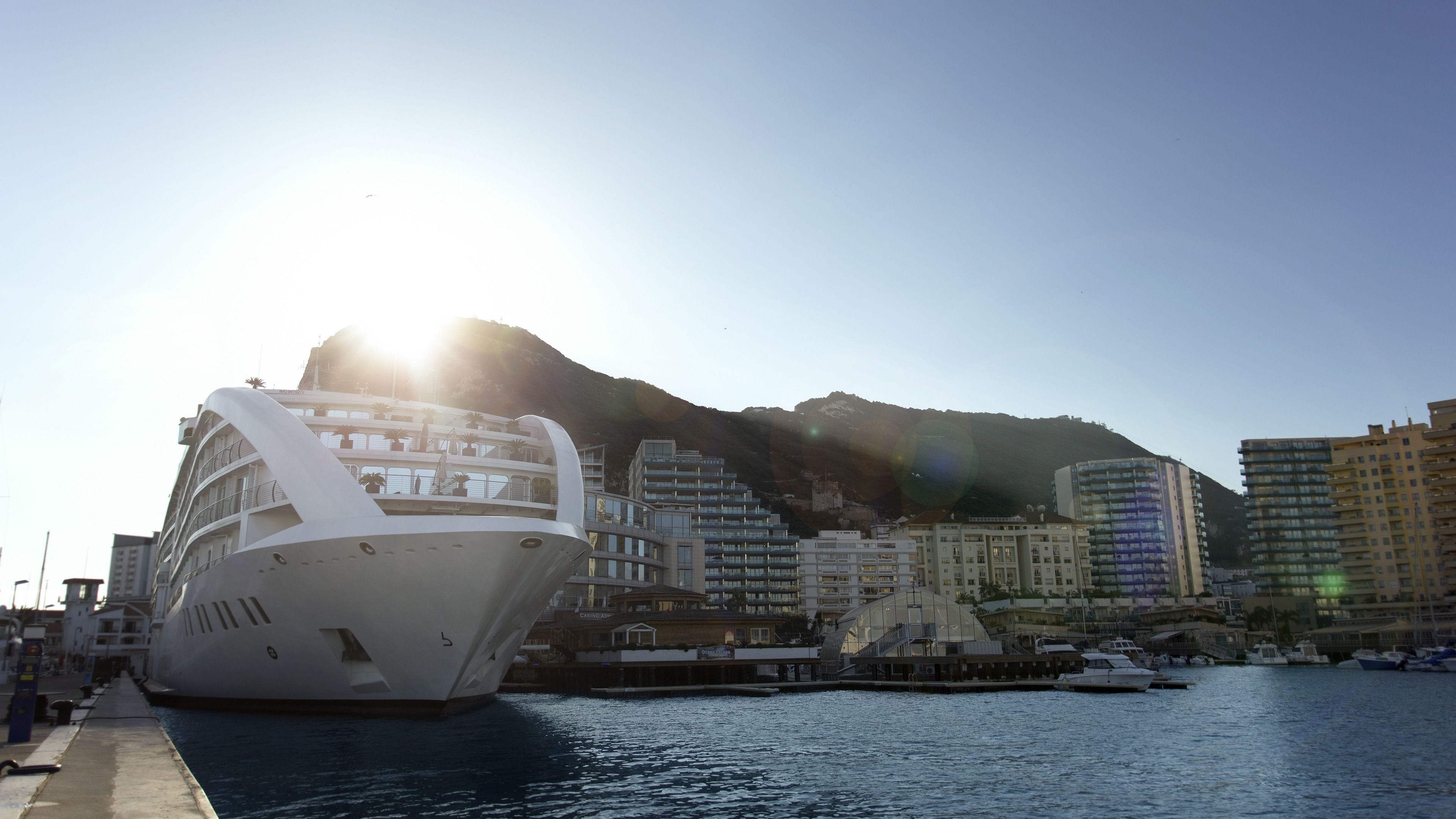 A cruise ship docked at a marina with a mountainous backdrop.