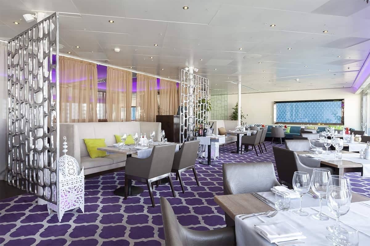 A modern restaurant with a purple patterned floor, white furniture, and a decorative white partition.