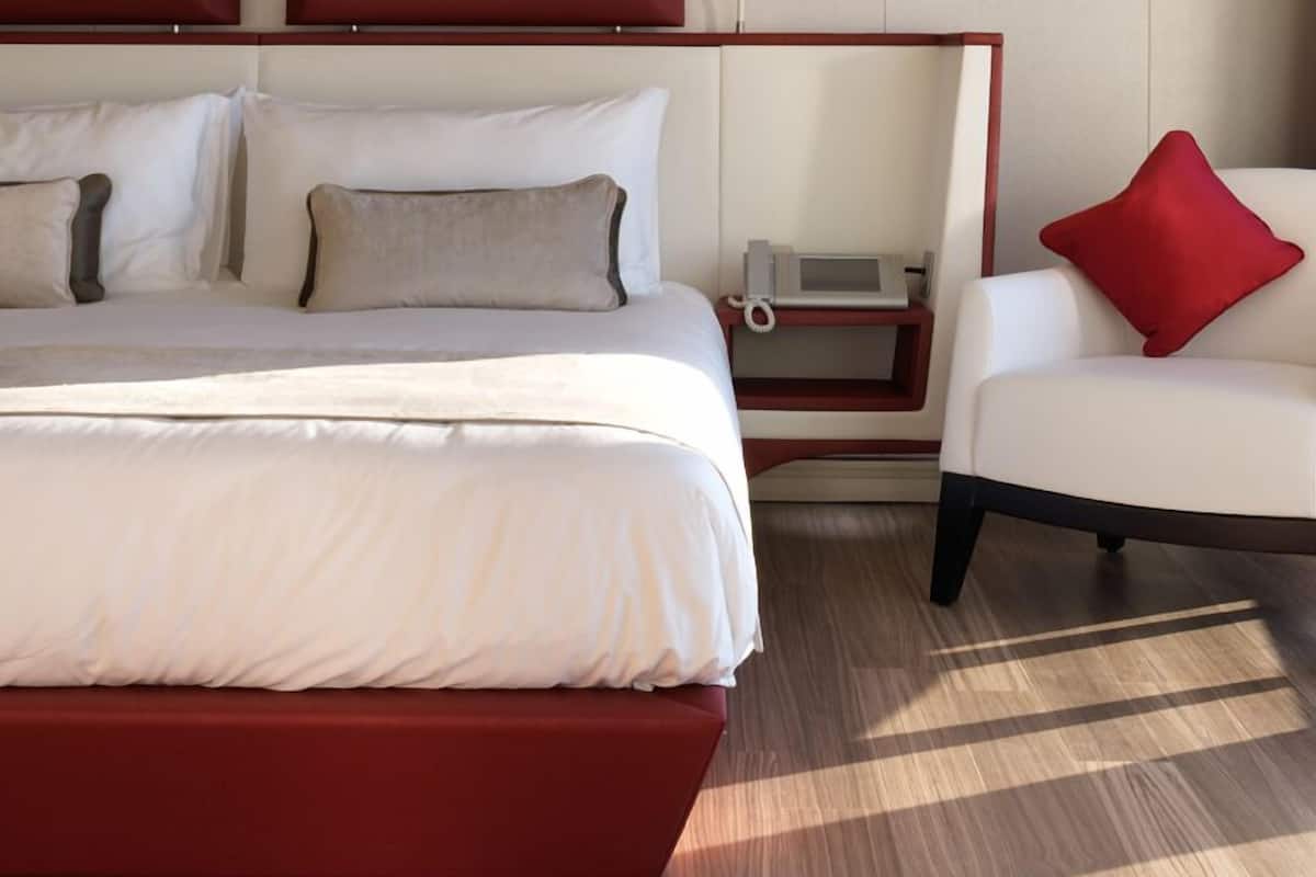 Ein modernes Hotelzimmer mit einem großen Bett, einem Nachttisch mit Telefon und einem roten Sessel.