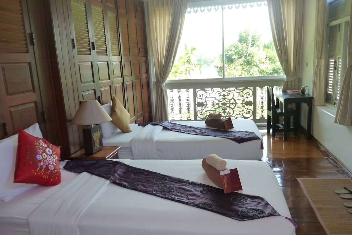 Habitación de hotel con dos camas, cabecero de madera, ventana con cortinas, una mesita y una silla.