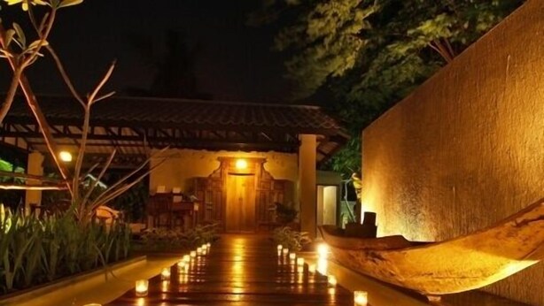 A wooden pathway lined with candles leading to a traditional building with a tiled roof. - The Legend Maeklong (Samut Songkhram)