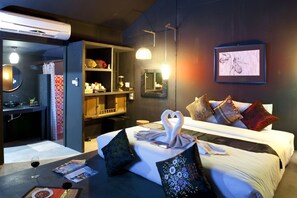 A hotel room with a bed, a desk with a chair, a mirror, a wardrobe, and a wall-mounted artwork. - The Legend Maeklong (Samut Songkhram)