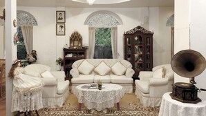 A traditional living room with a white sofa, matching armchairs, a round coffee table, and a gramophone. - The Legend Maeklong (Samut Songkhram)