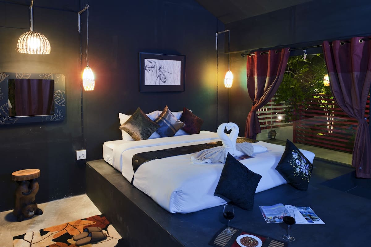 Un dormitorio moderno con una cama grande, una mesita de noche, un taburete pequeño y una ventana con cortinas.