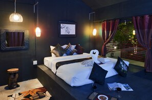 A modern bedroom with a large bed, a bedside table, a small stool, and a window with curtains.