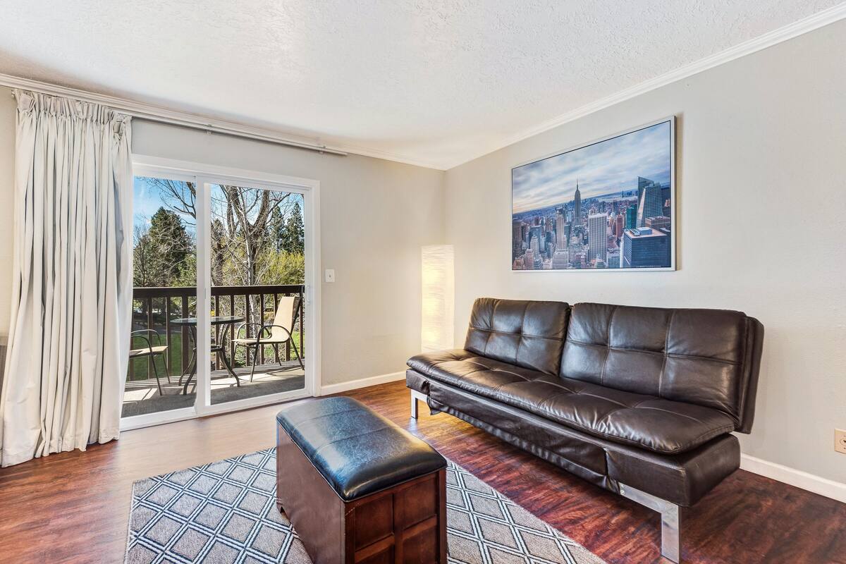 A living room with a leather sofa, a bench, and a cityscape painting on the wall.