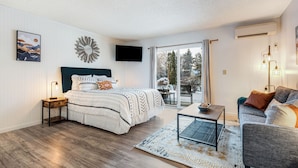 A modern bedroom with a bed, bedside table, and a view of the outdoors. - Pioneer Park Rentals (Bend)