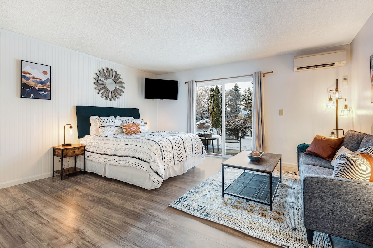 A modern bedroom with a bed, bedside table, and a view of the outdoors.