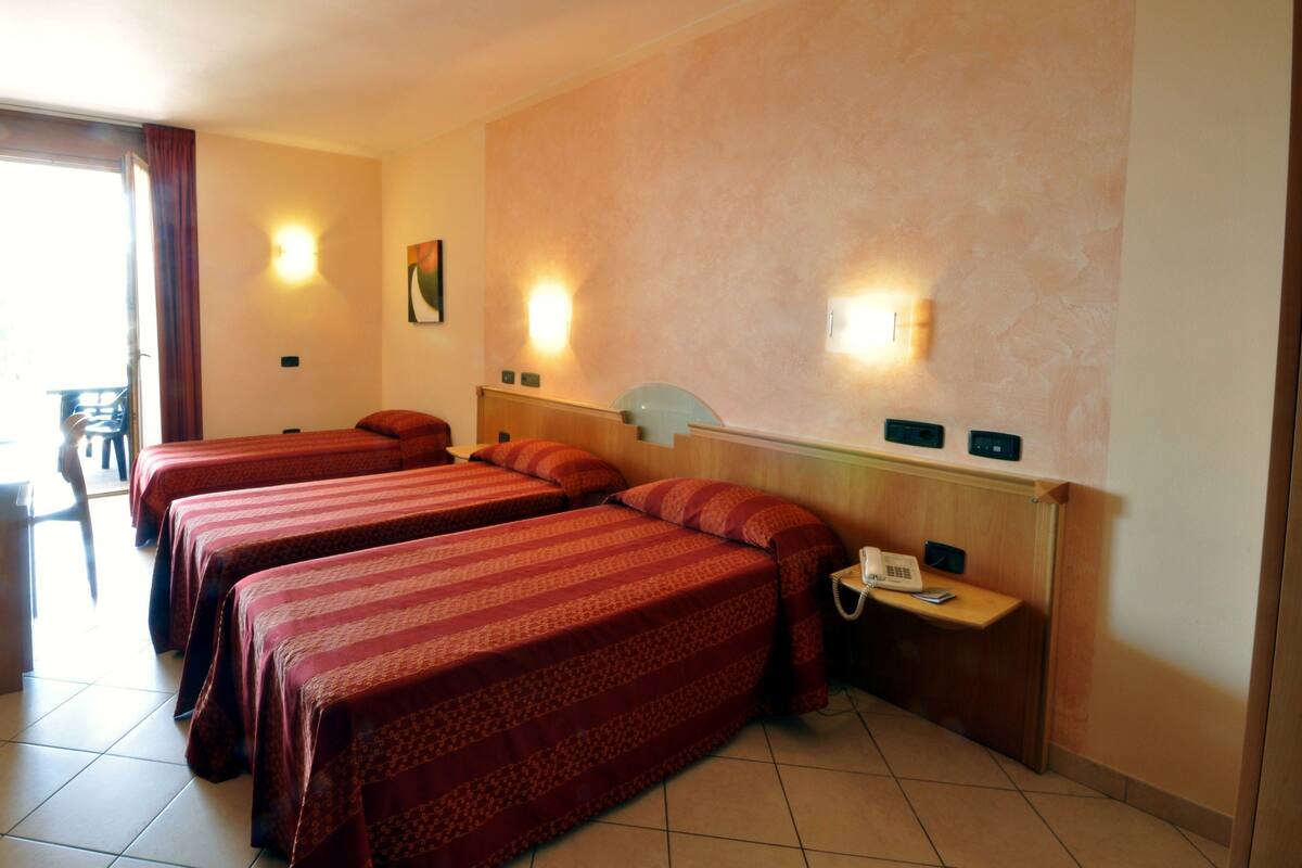 Habitación de hotel con tres camas, un escritorio y un teléfono, y dos lámparas fijadas a la pared.