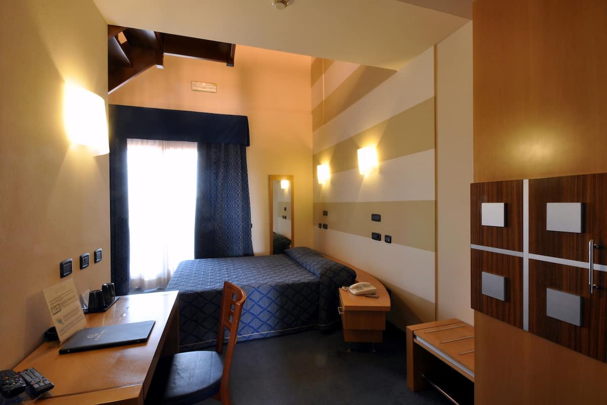 Habitación de hotel con cama, escritorio, silla y armario con varios compartimentos.