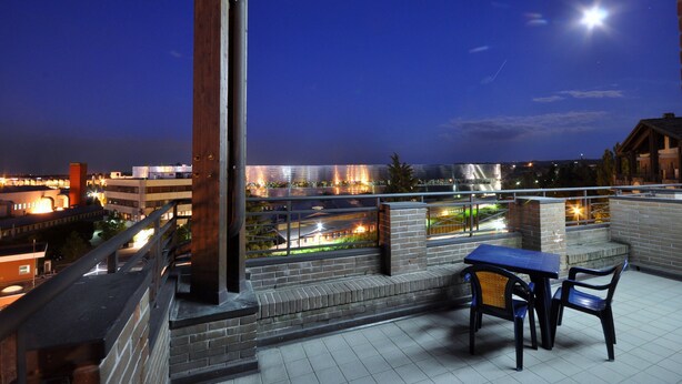 A rooftop terrace with a table and chairs, overlooking a cityscape at night. - Planet Hotel (Maranello)