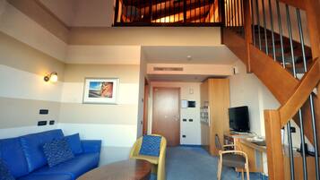 Una sala de estar con un sofá azul, una mesa de centro de madera, una silla amarilla pequeña, un televisor y una escalera.