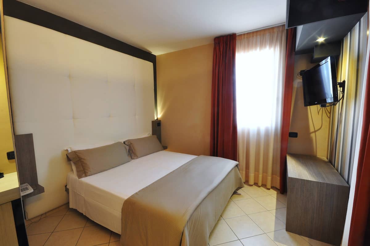 Habitación de hotel con cama, televisor montado en la pared y ventana con cortinas.