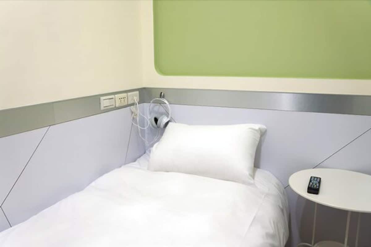 Ett hotellrum med en säng, ett sängbord, ett eluttag och en grön vägg.