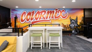 A restaurant with a mural of a cityscape and a large 'Colormio' sign. There are two white bar stools with green cushions. - ColorMix Hotel & Hostel (Taipei)