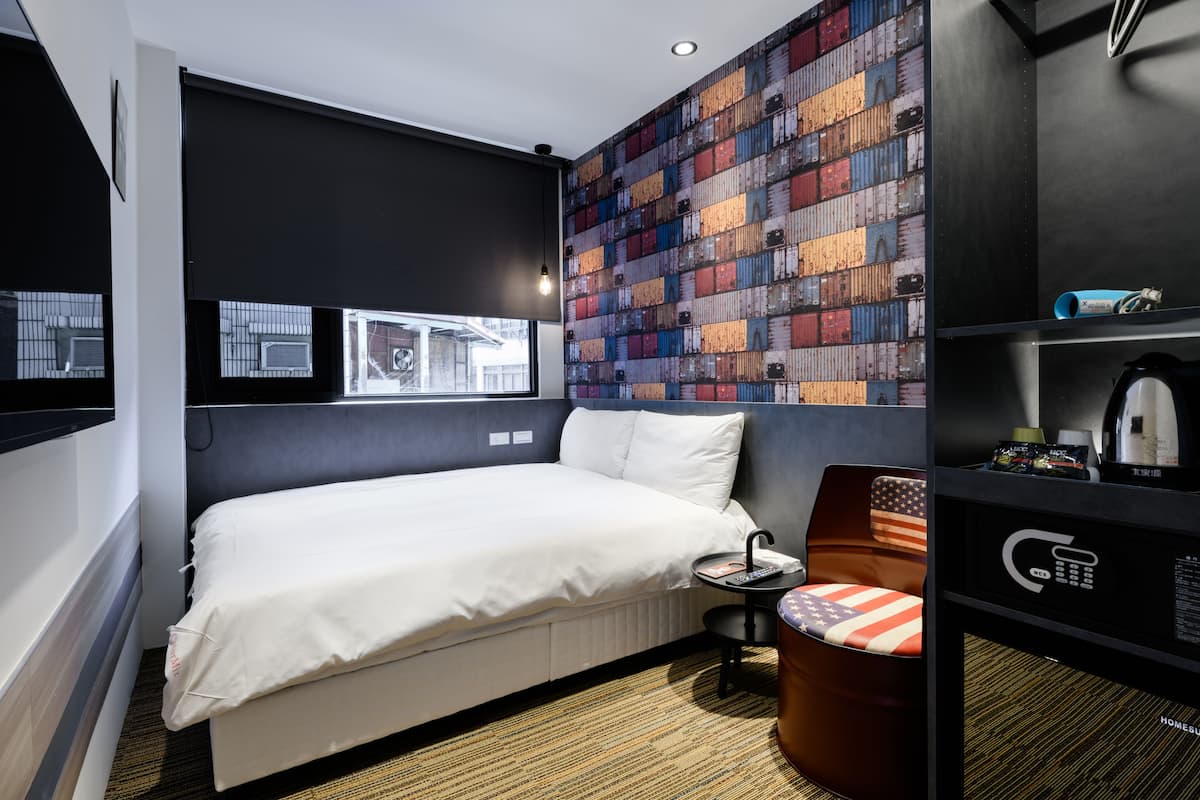 Ett modernt hotellrum med en stor säng, en liten sittgrupp, en vägg dekorerad med fraktcontainrar och ett fönster med utsikt över omgivningen.