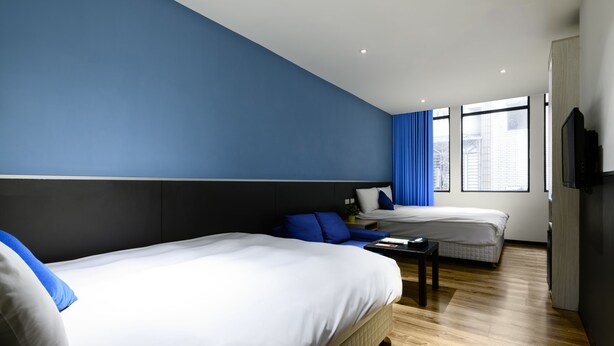 A modern hotel room with two beds, a flat-screen TV, and large windows with blue curtains. - ColorMix Hotel & Hostel (Taipei)