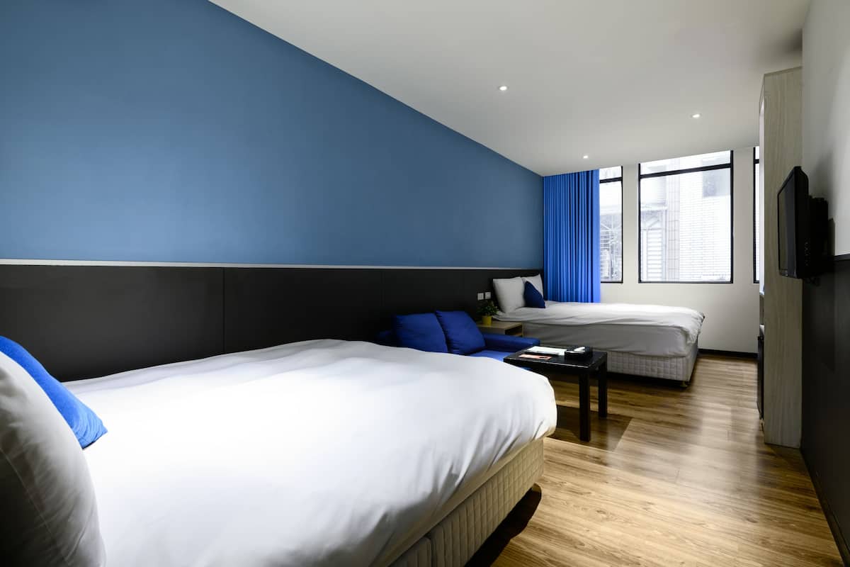 Ett modernt hotellrum med två sängar, en platt-TV och stora fönster med blå gardiner.