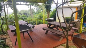 An outdoor patio with picnic tables and a barbecue grill, surrounded by greenery and a view of the landscape. - Dreaming Forest (Seogwipo)
