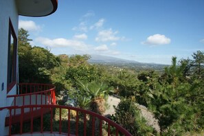 A balcony with a red railing overlooking a lush landscape with trees and distant mountains. - Dreaming Forest (Seogwipo)