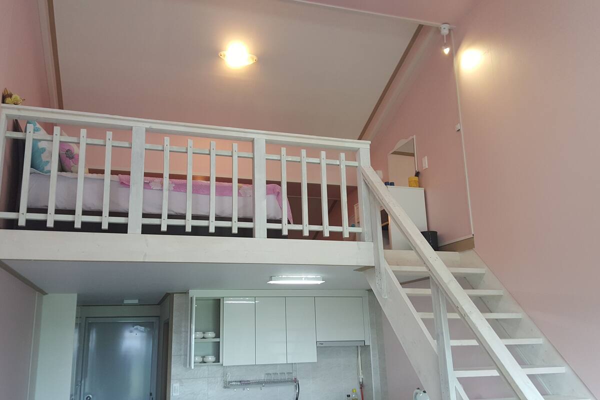 A room with a bunk bed, a staircase, and a kitchen area.