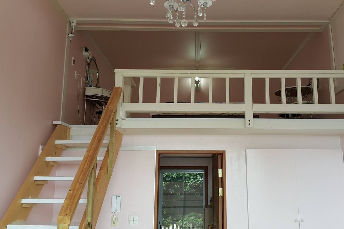 A room with a bunk bed, a wooden ladder, a chandelier, and a door with a window.